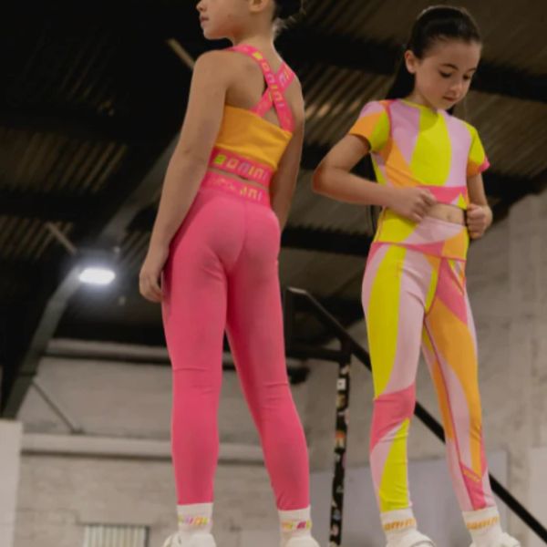 Two young girls in colorful athletic wear indoors.