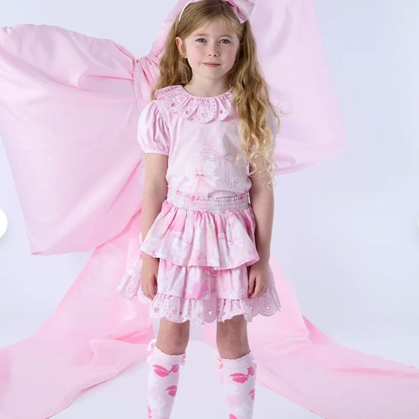 Young girl in a pink outfit with long wavy hair and a headband.
