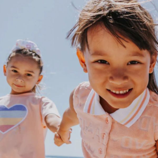 Two young girls holding hands and smiling outdoors.