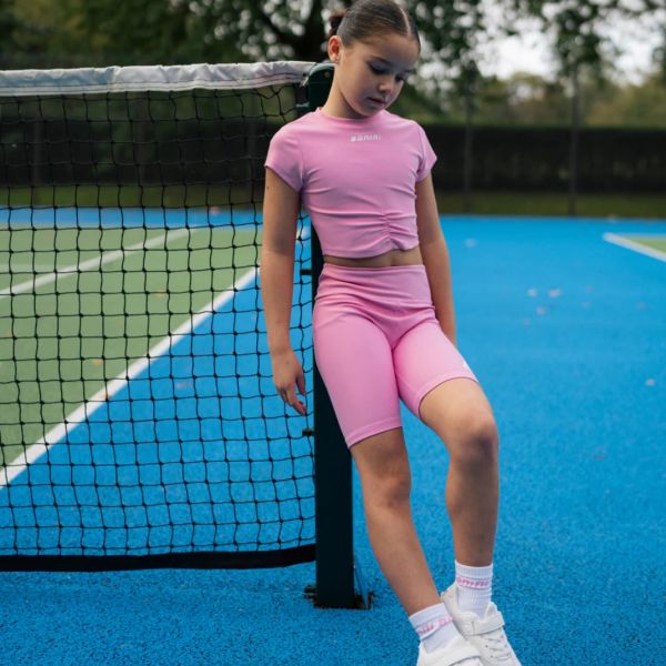 Young girl in pink sportswear leaning on a tennis net.