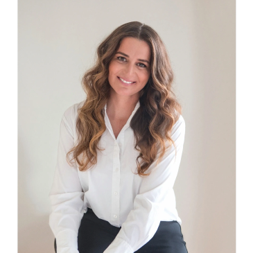 Smiling woman with long wavy hair in a white blouse and black pants.