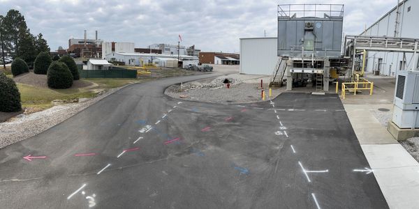 Industrial site with directional markings on asphalt under cloudy sky.