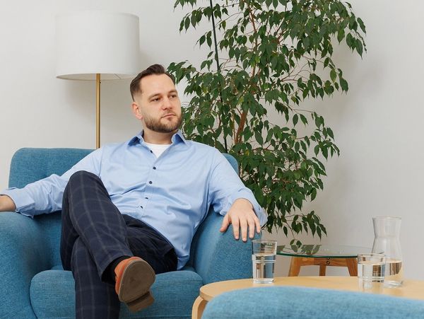 Man in blue shirt sitting thoughtfully in a cozy living room.