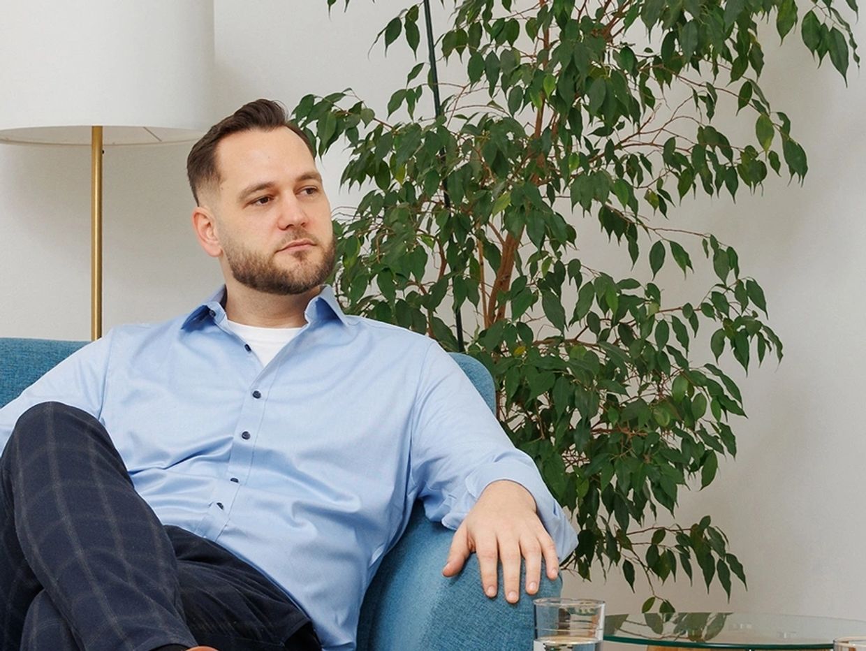 Man in blue shirt sitting on a couch, looking thoughtful.