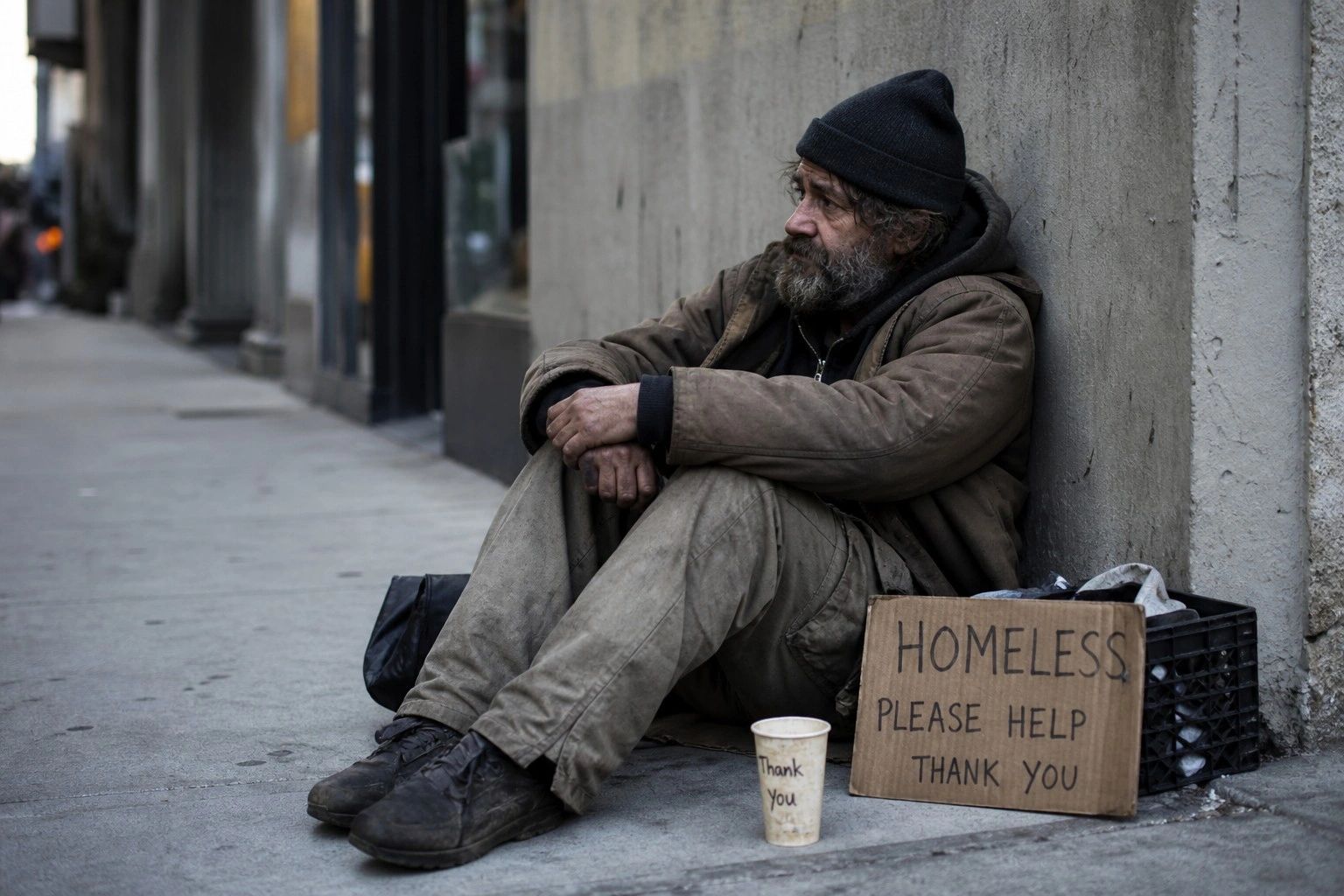 Homeless man sitting on the sidewalk with a sign asking for help.
