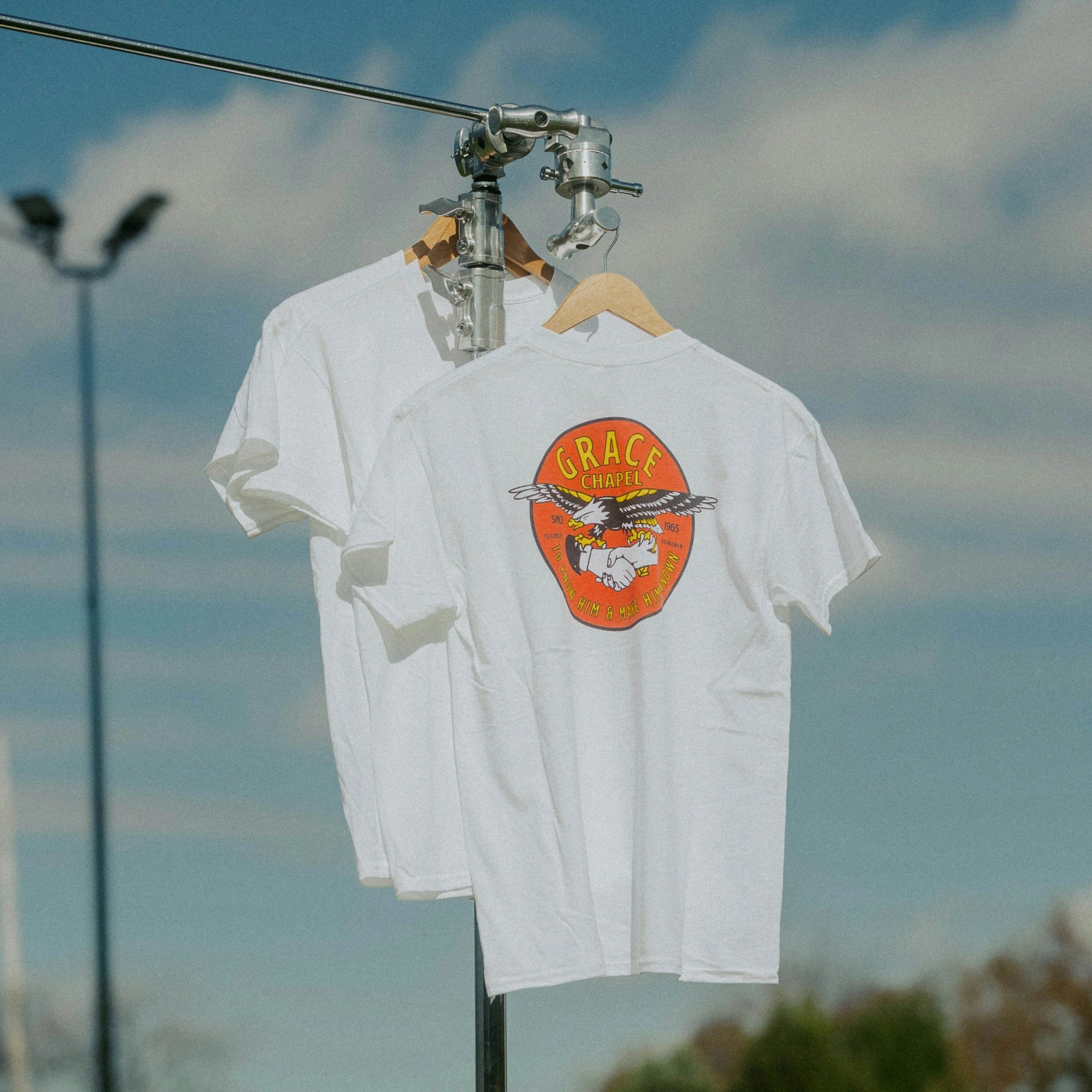 White t-shirts hanging on a metal rod outdoors.