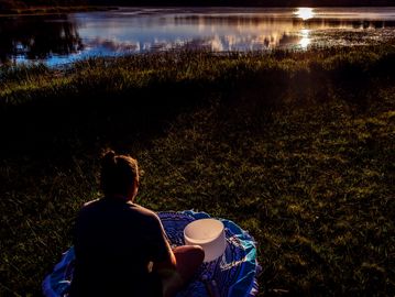 Person sitting by a lake during sunset.