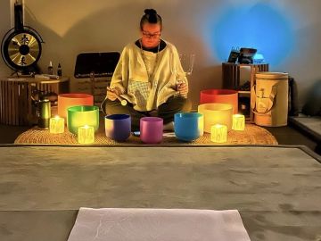Person meditating with colorful bowls and candles.