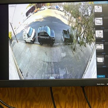 CCTV monitor showing parked vehicles on a street with license plate detection.