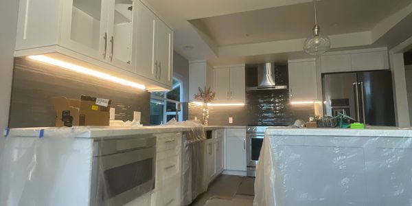 Modern kitchen with white cabinets and protective plastic covers on countertops and appliances.