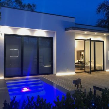 Modern house with illuminated pool and open glass doors at dusk.