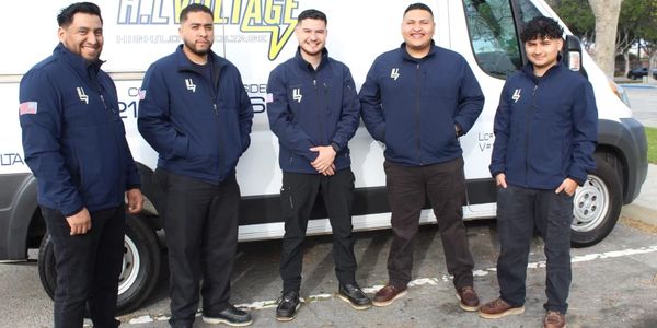 Five men in matching jackets stand in front of a van labeled H.L. Voltage.