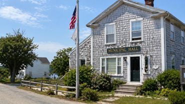 A quaint municipal hall building with an American flag in front on a sunny day.