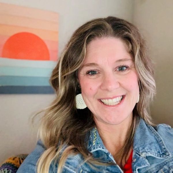 Smiling woman with wavy hair in denim jacket.