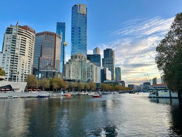 City skyline with river and boats during sunset under a partly cloudy sky.