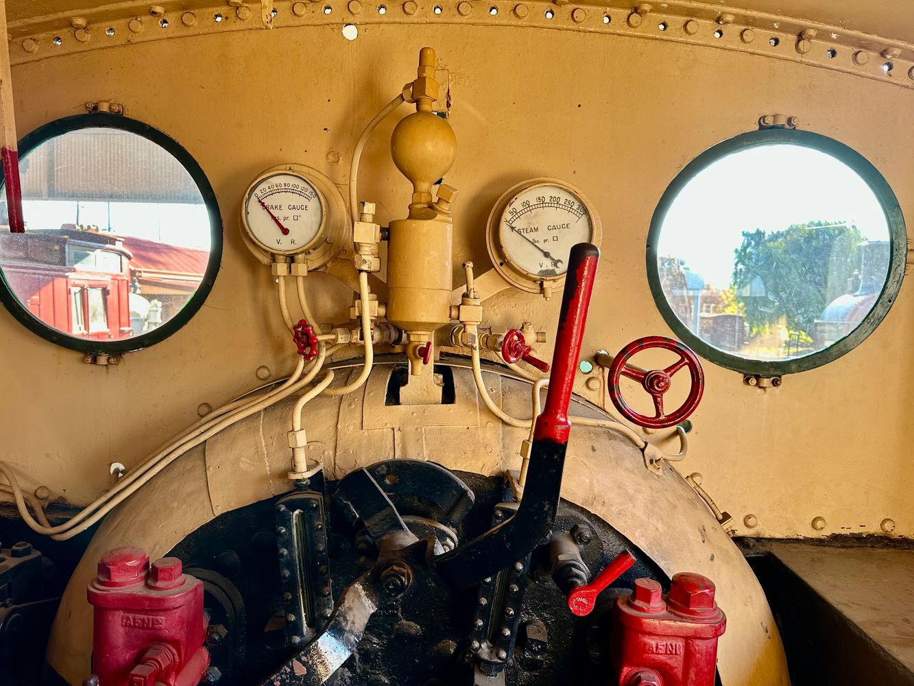 Vintage train control panel with gauges and red levers inside a cabin.