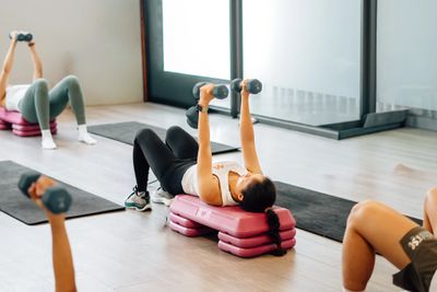 People exercising with dumbbells on mats in a bright gym.