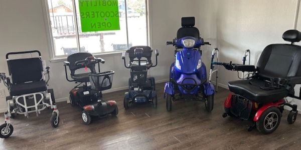 Various mobility scooters and wheelchairs lined up indoors.