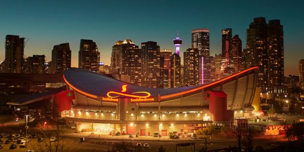Night view of Scotiabank Saddledome with city skyline.