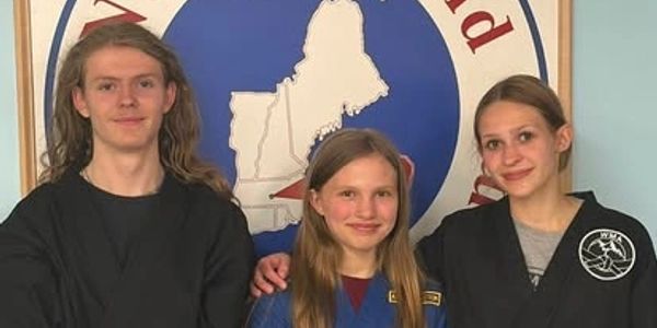 Three youths posing indoors with a blue and red emblem background.