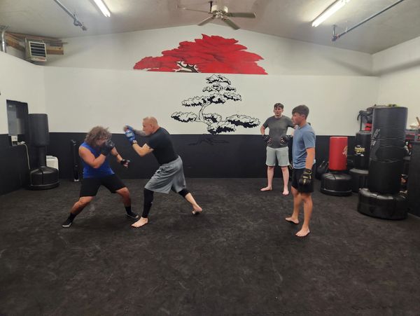 Two men sparring while two others watch in a martial arts gym.