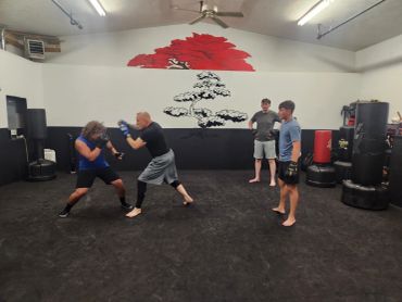 Two men sparring while two others watch in a martial arts gym.