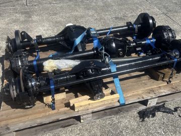 Several automotive axles secured with blue straps on a wooden pallet.