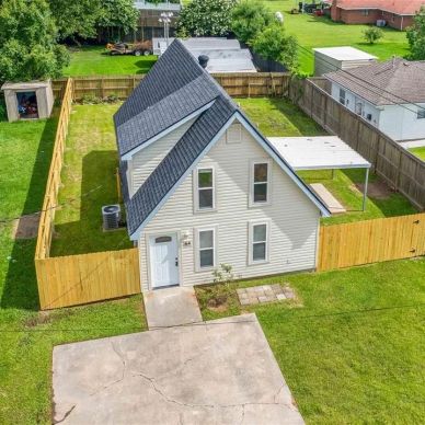 A white house with a fenced backyard and black roof.