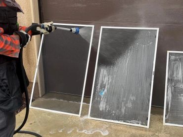 Person cleaning window screens with a hose.