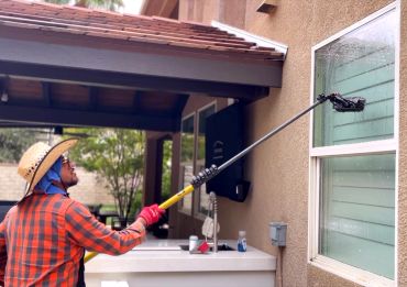 Man cleaning window with a long brush outdoors.
