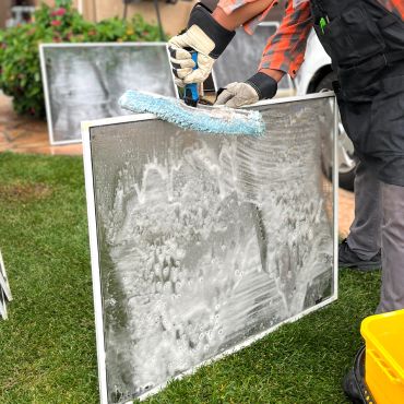 Person cleaning a soapy window screen outdoors.