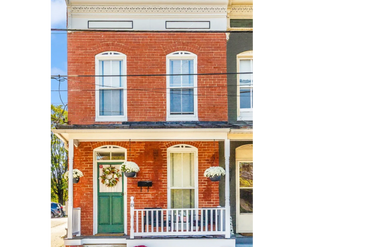 Charming brick townhouse with green door, white trim, and flower decorations on porch.
