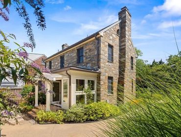 Charming stone house with lush garden and clear blue sky.