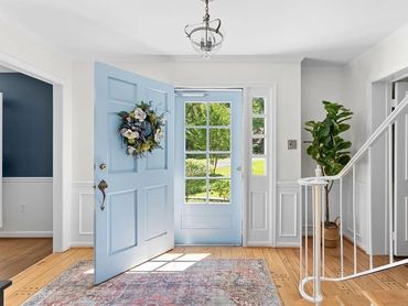 Bright entryway with light blue door, floral wreath, and wooden floor.