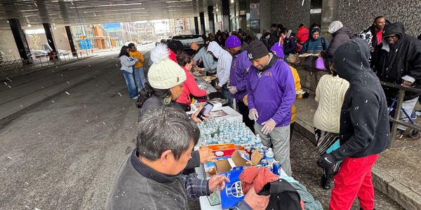 People distributing food and drinks under a bridge.