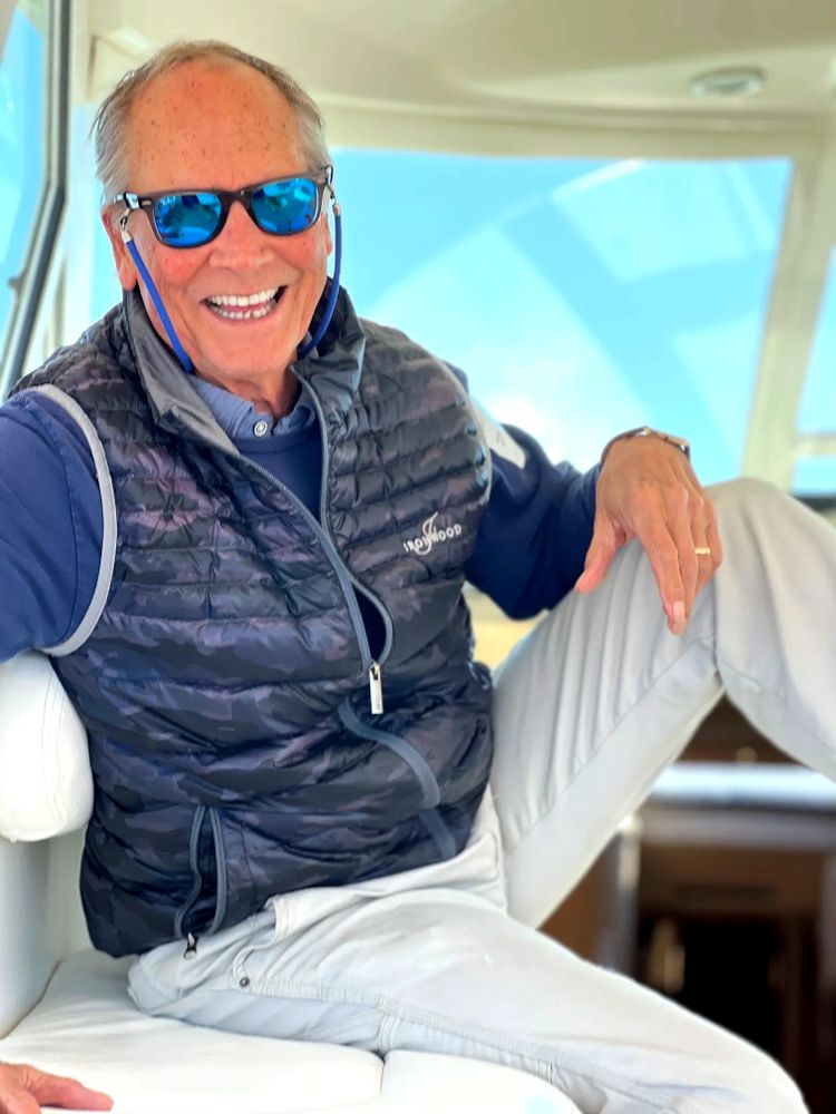 Smiling older man wearing sunglasses and a vest, relaxing indoors.