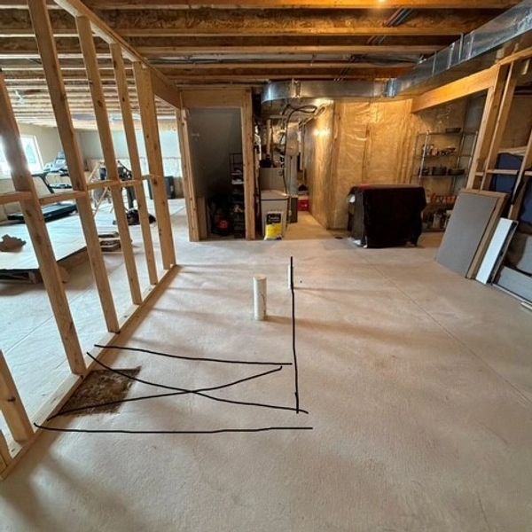 Unfinished basement with exposed framing and plumbing pipe on concrete floor.