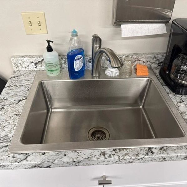 Clean stainless steel kitchen sink with soap and sponge on granite countertop.