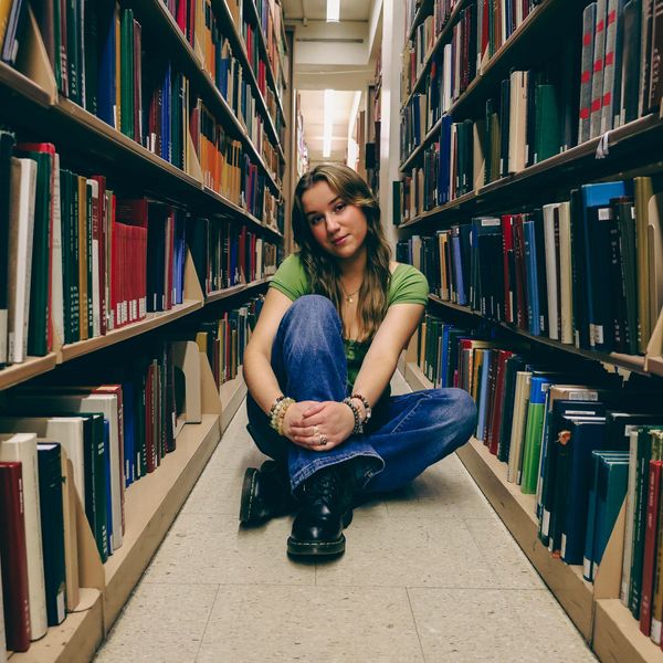 Young woman sitting on library floor between bookshelves.