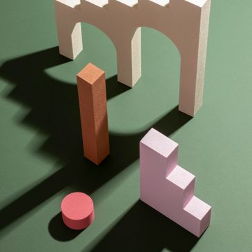 Geometric shapes casting shadows on a green surface with a white arch structure.