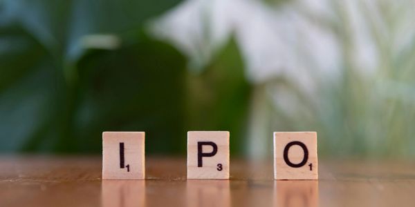 Scrabble tiles spelling "IPO" on a wooden surface with green background.