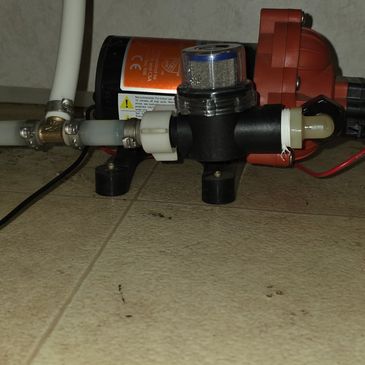 Close-up of a water pump system connected to pipes on a tiled floor.