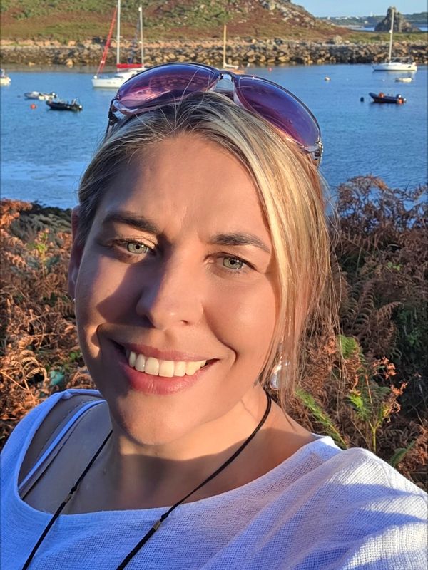 Woman smiling outdoors near a body of water.