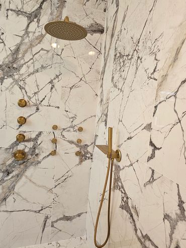Luxurious marble shower with gold fixtures and a handheld showerhead.