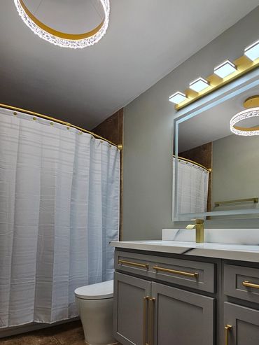 Modern bathroom with gold fixtures and grey cabinetry.