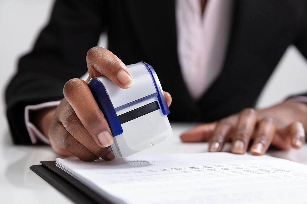Person stamping a document on a desk, dressed in professional attire.