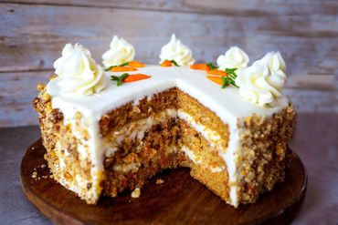 A delicious carrot cake with cream cheese frosting and walnut coating on a wooden board.