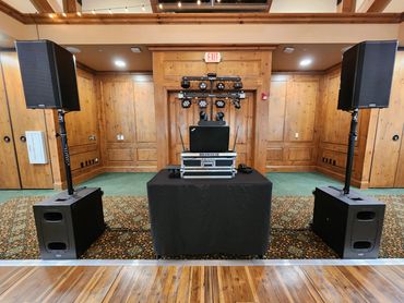 DJ setup with speakers, lighting, and equipment in a wood-paneled room.