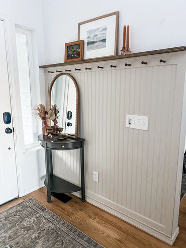 Elegant entryway with a black console table, decorative mirror, and framed art on beige beadboard wa
