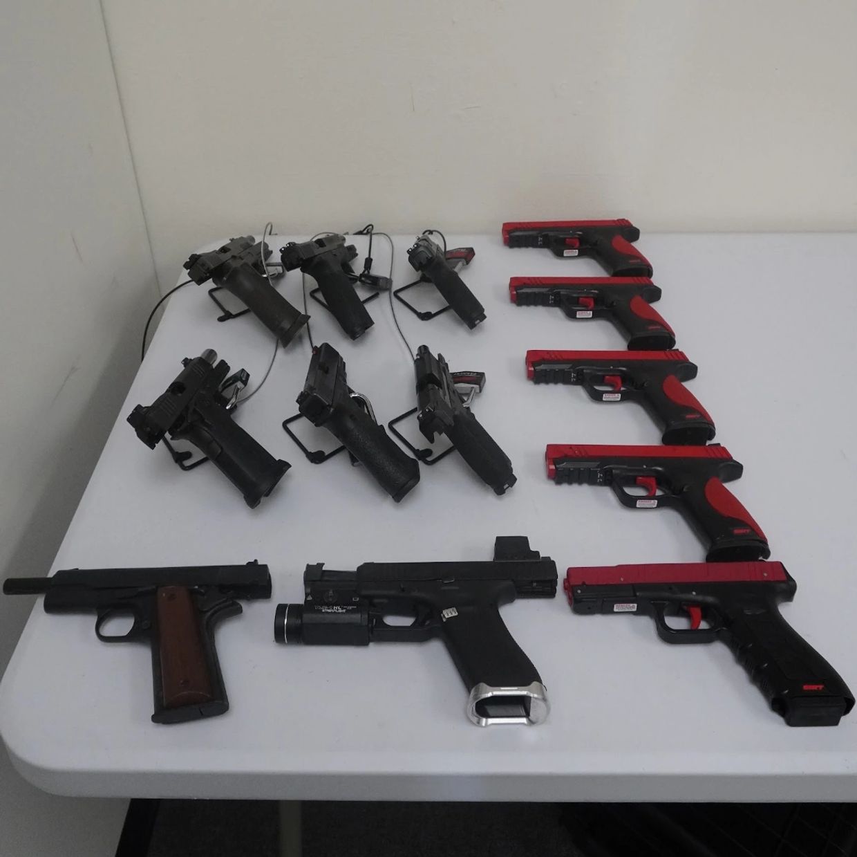 Various black and red toy guns arranged on a white table.